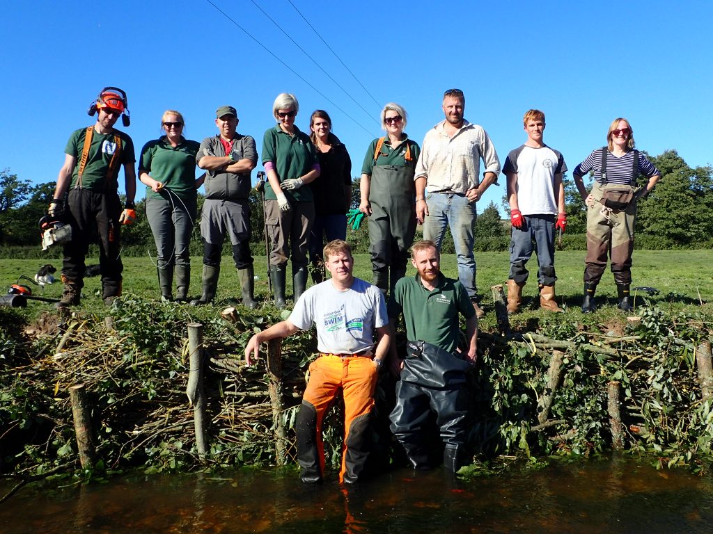 A group of volunteers posing with completed willow structure to repair river bank erosion