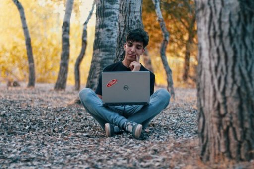 man sat in the woods with his legs crossed and a laptop balanced on is knees
