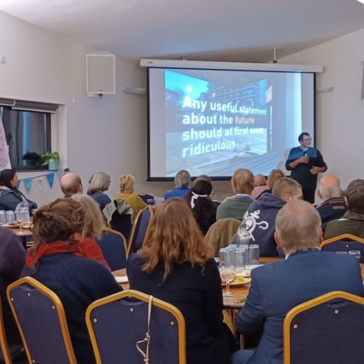 A group of people seated at tables looking at a presenter and projector screen