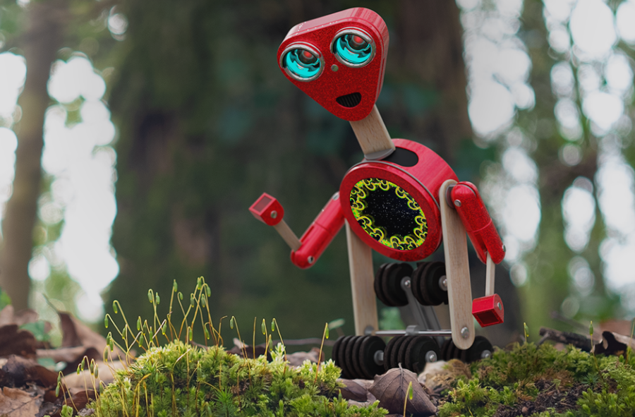 Small red robot exploring next to moss and a tree